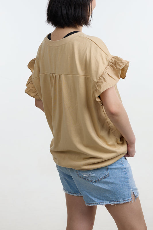 Person wearing a beige ruffled top and denim shorts on a white background