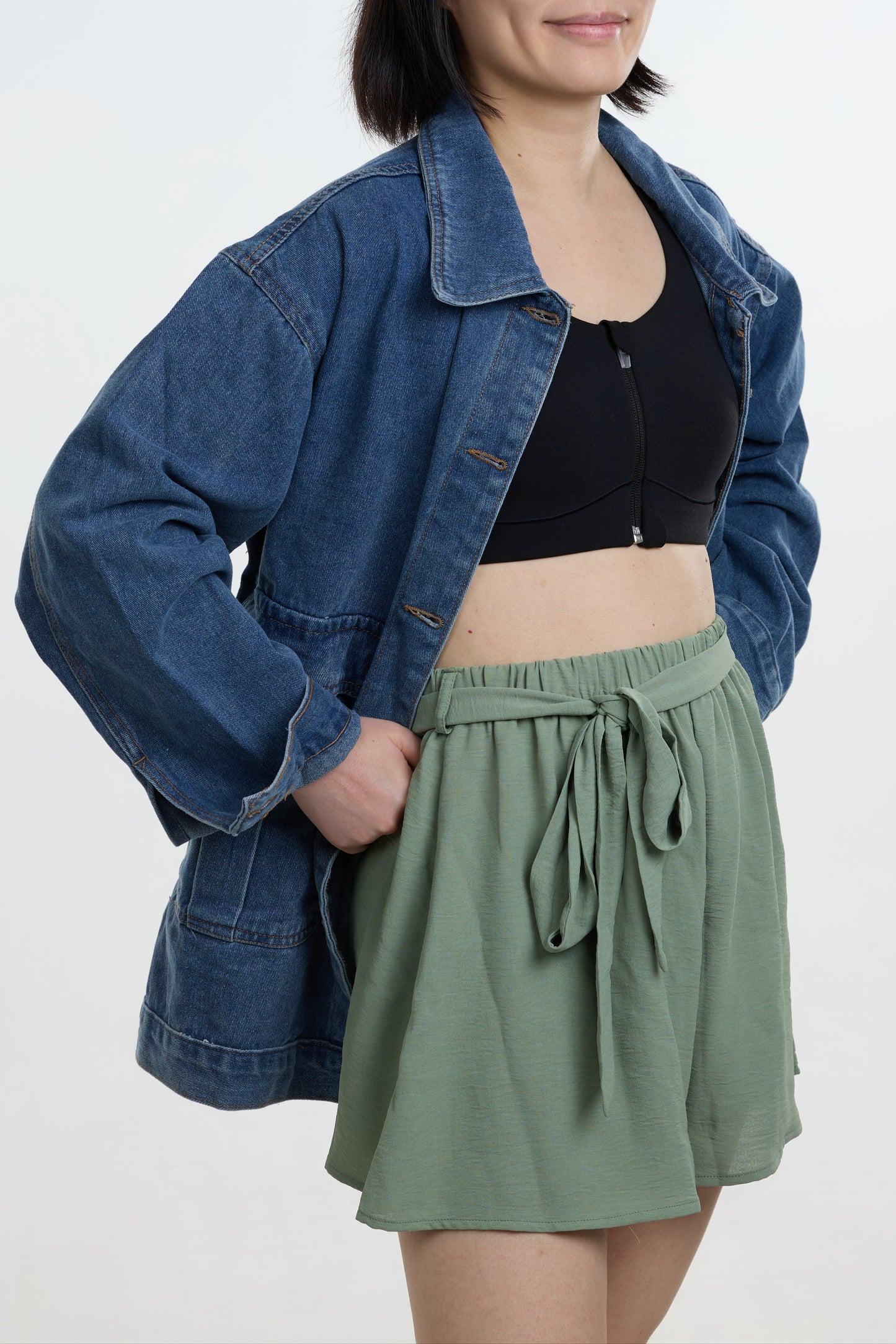 Woman wearing a denim jacket, black top, and green shorts on a white background