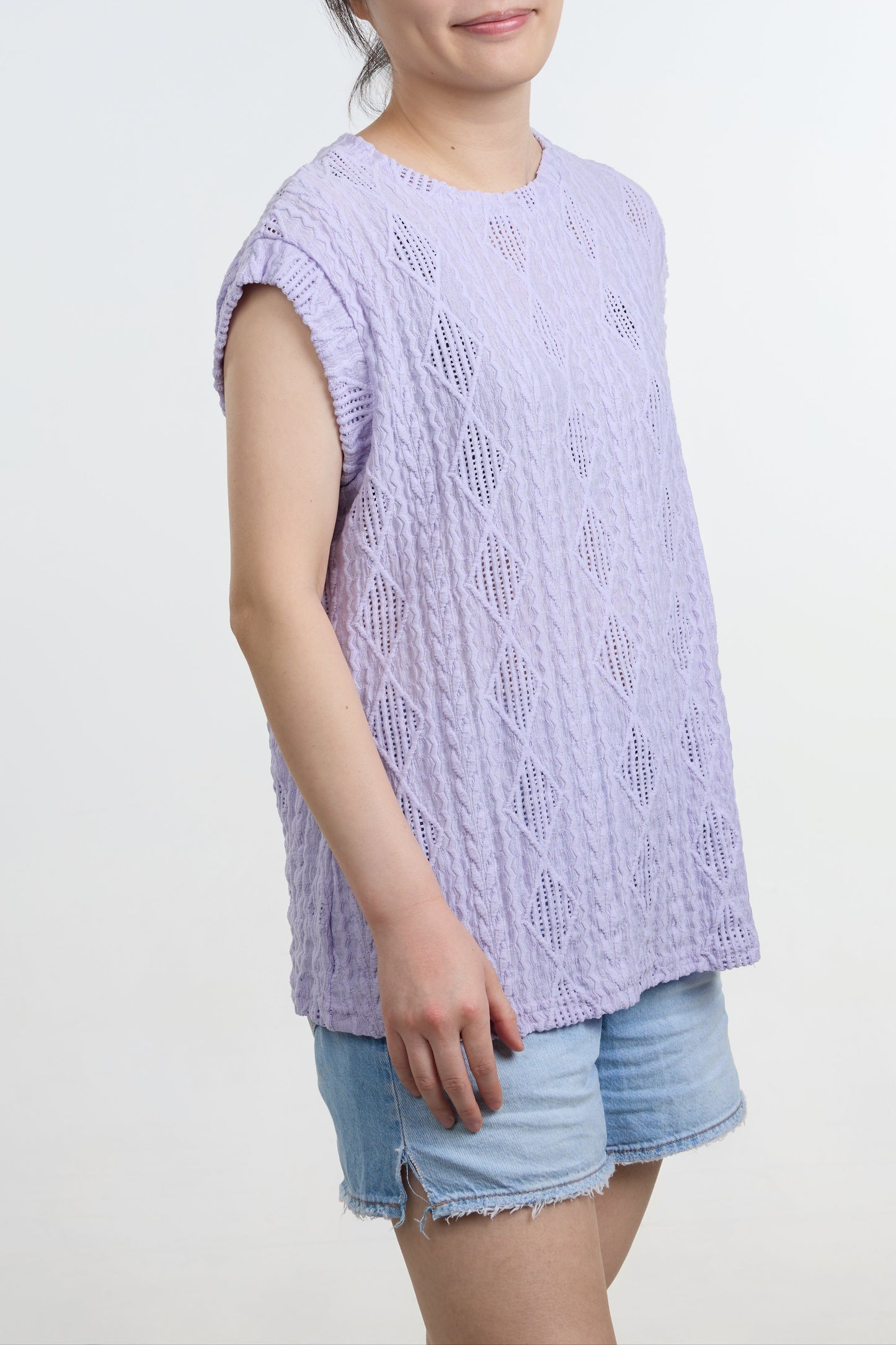 Woman wearing a light purple sleeveless top and denim shorts on a white background