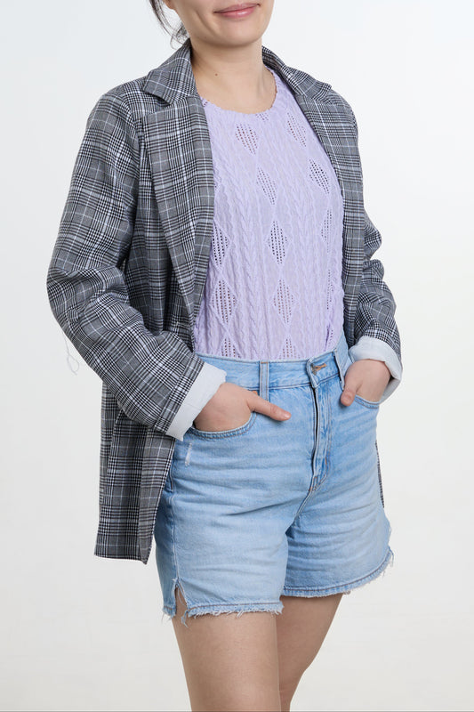Woman wearing a checkered blazer, light purple sweater, and denim shorts on a white background