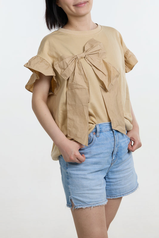 Woman wearing a beige top with ruffled sleeves and denim shorts on a white background